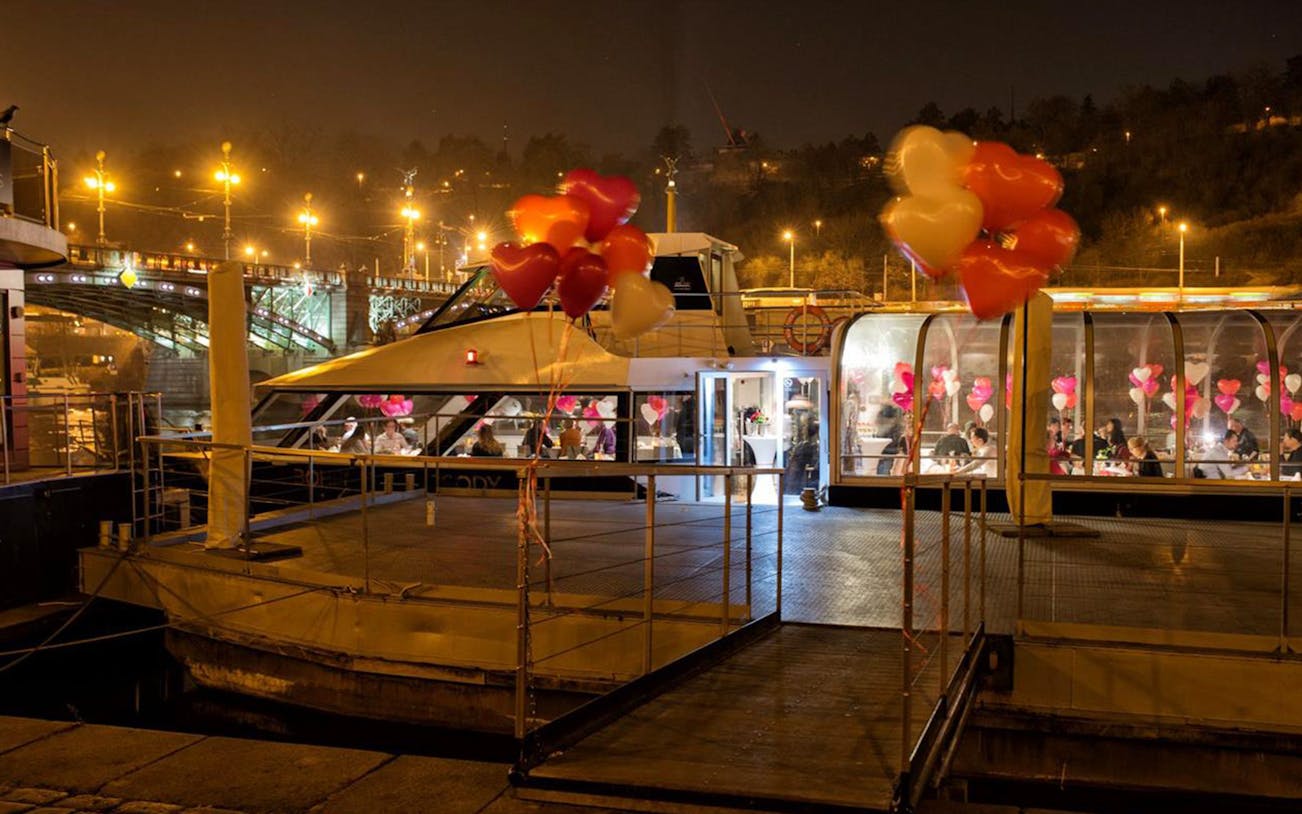 Romantic dinner cruise with heart balloons and live music on a river at night.
