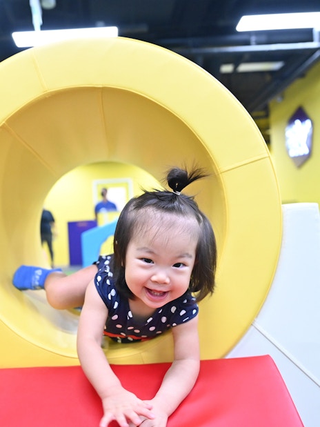 Child playing in a yellow tunnel at SuperPark Singapore indoor playground.