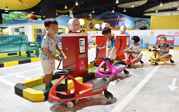 Children playing at Tayo Station's mini gas station with ride-on cars.