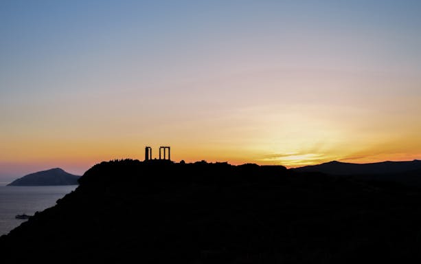 Temple of Poseidon at Cape Sounion silhouetted against a sunset.
