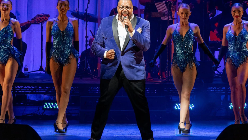 Performer singing with dancers in a West End musical show.