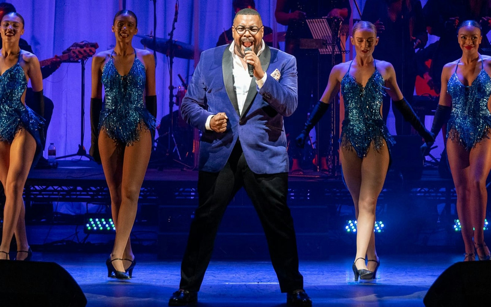 Performer singing with dancers in a West End musical show.