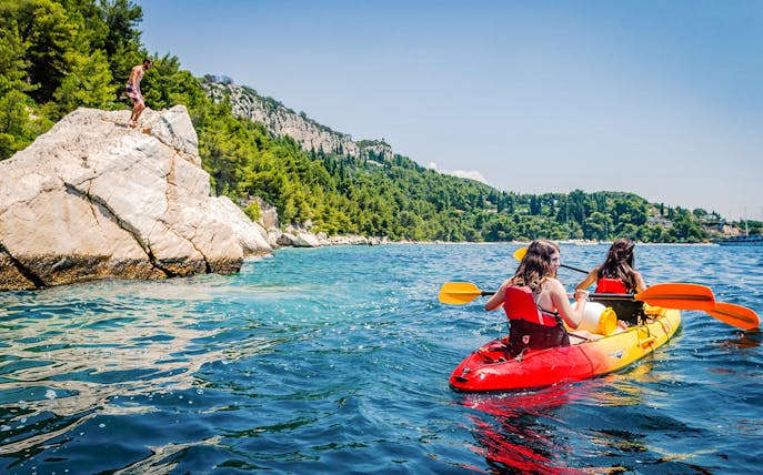 Kayakers paddling near rocky coastline on a sea kayaking tour from Split.
