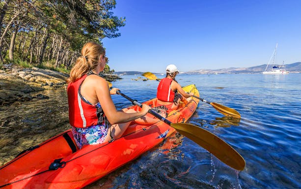 Sea kayaking near Split with two people paddling along a rocky coastline.