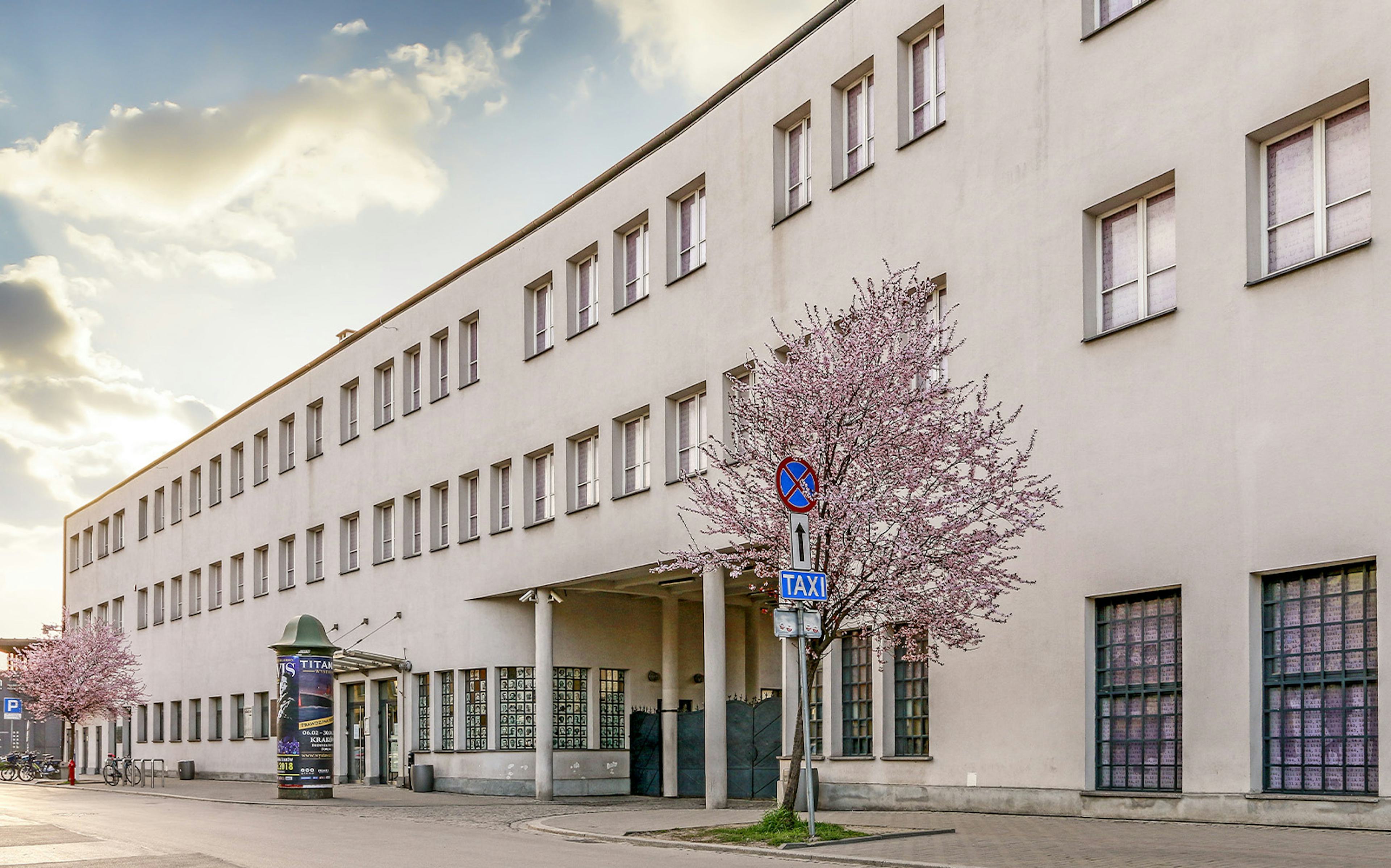 Schindler's Factory exterior in Krakow with blooming trees nearby.