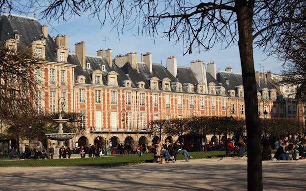 Place des Vosges in Le Marais, Paris, with people relaxing in the park.