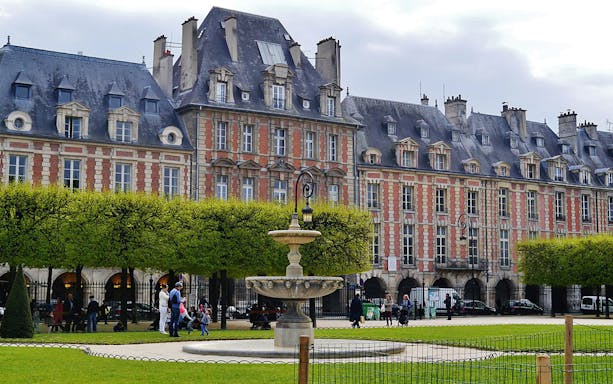 Place des Vosges with fountain and people walking, Le Marais, Paris.