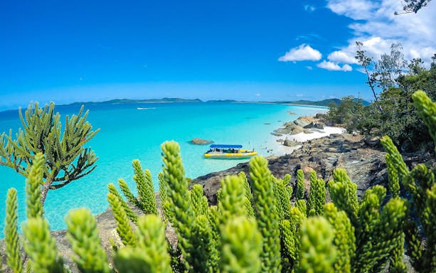 Whitsundays beach with turquoise water and a yellow raft near rocky shore.