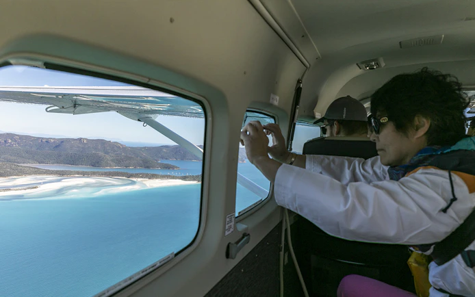 Passenger photographing Whitsundays from scenic flight window.