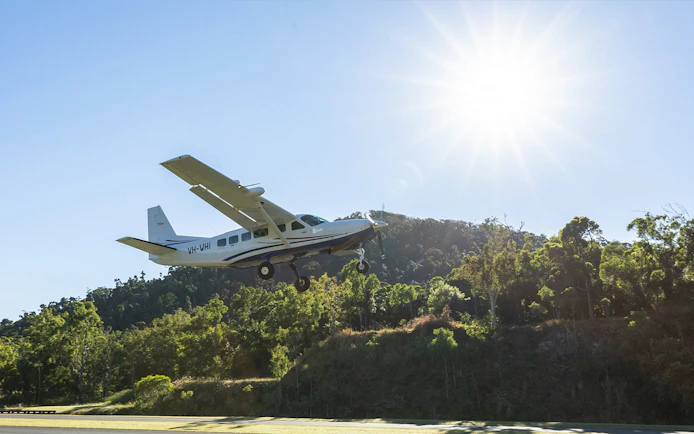 Small plane taking off for Whitsundays scenic flight over lush green landscape.