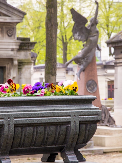 Stone planter with colorful flowers in Montparnasse Cemetery, Paris.