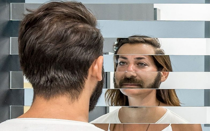 Person viewing fragmented reflection in mirror exhibit at Museum of Illusions.