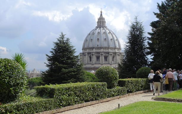 Vatican Gardens with St. Peter's Basilica dome in background, group of tourists walking.