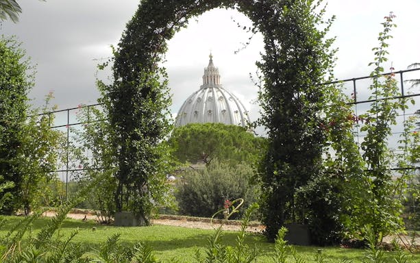 Vatican Gardens archway with St. Peter's Basilica dome in the background.
