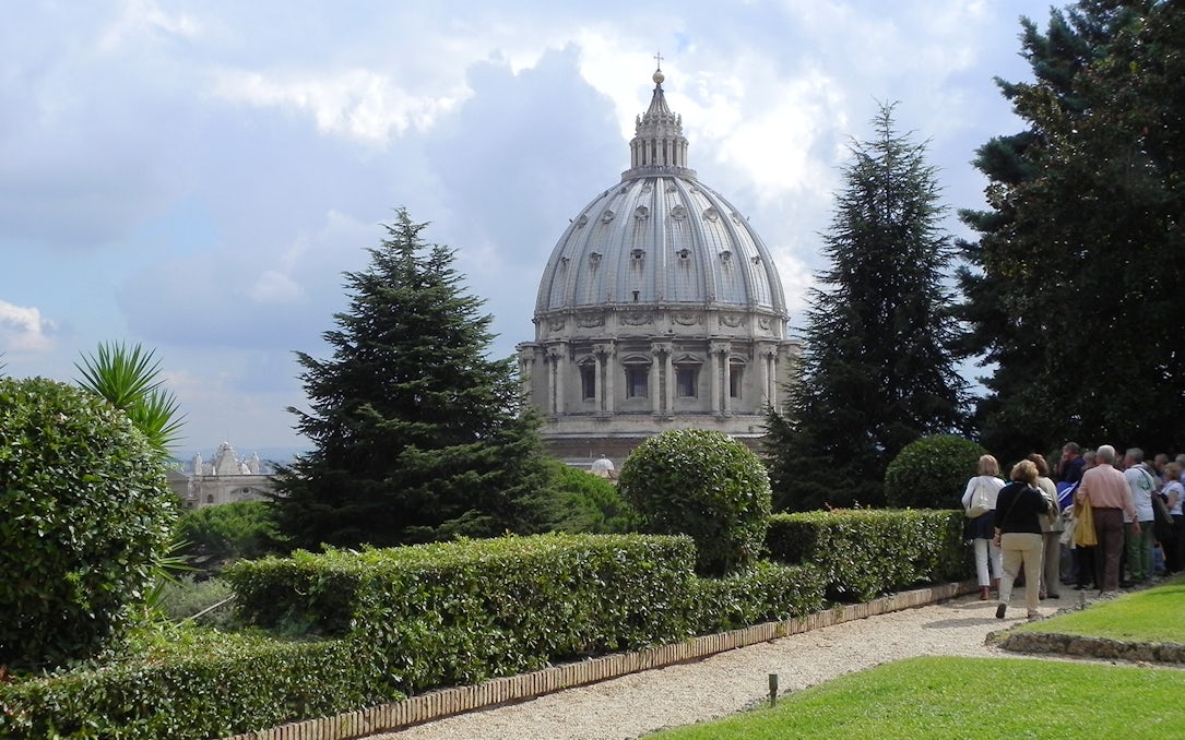 Vatican Gardens with view of St. Peter's Basilica dome, group of tourists exploring.