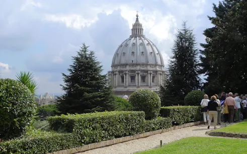 Vatican Gardens with view of St. Peter's Basilica dome, group of tourists exploring.