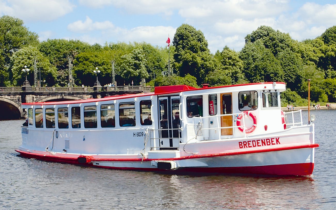 Tour boat on Alster River in Hamburg with bridge and trees in background.