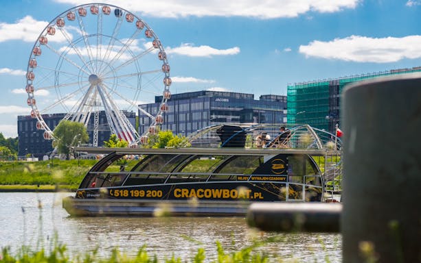 Cruise boat on Vistula River with Ferris wheel in Krakow's former Jewish Ghetto.