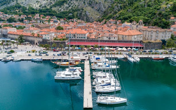 Speedboats docked at Kotor Bay marina with historic town and mountains in the background.