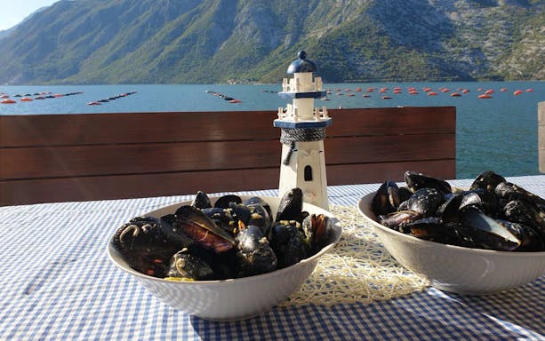 Bowls of mussels on a table with Kotor Bay and mountains in the background.