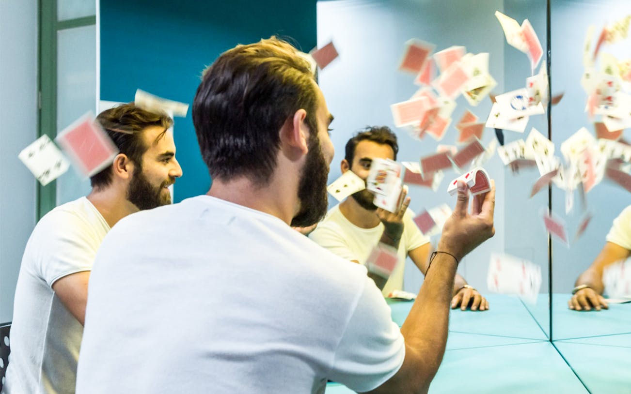 Man interacting with mirror illusion and playing cards at Museum of Illusions, Thessaloniki.