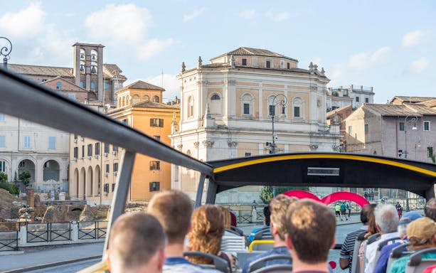 Open-top bus tour passing historic buildings in Rome.