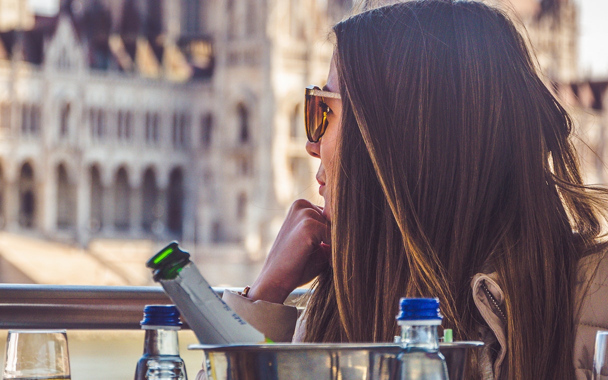 Woman enjoying Budapest Party Boat Cruise with drinks, Hungarian Parliament in background.