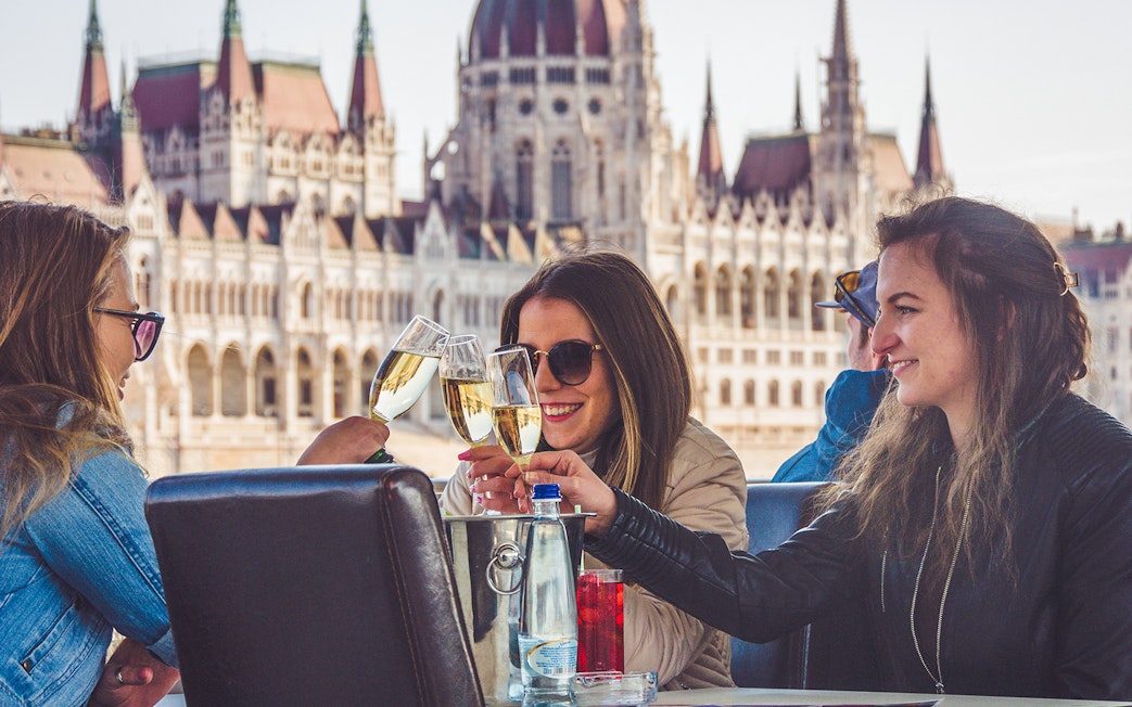 Friends toasting on a Budapest party boat cruise with the Hungarian Parliament in the background.