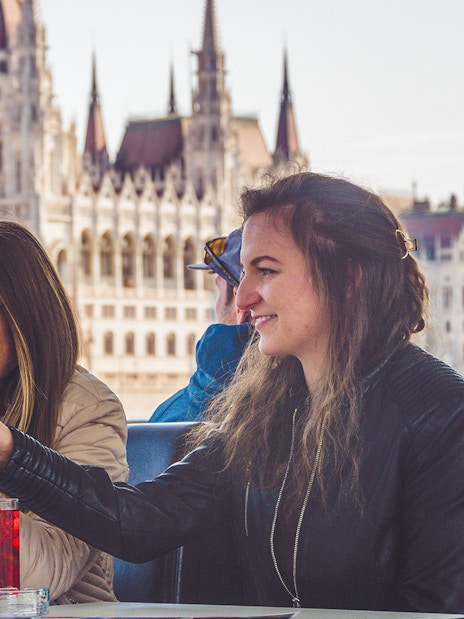 Friends toasting on a Budapest party boat cruise with the Hungarian Parliament in the background.