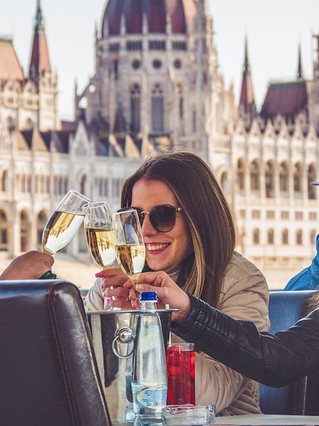Friends toasting on a Budapest party boat cruise with the Hungarian Parliament in the background.
