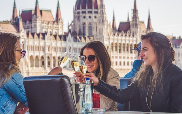 Friends toasting on a Budapest party boat cruise with the Hungarian Parliament in the background.
