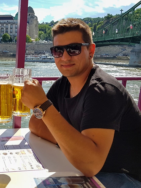 Couple enjoying beers on a Budapest party boat cruise with cityscape view.