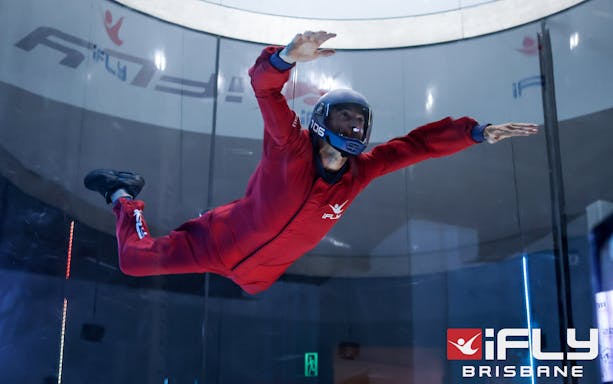Indoor skydiver in red suit at iFly Brisbane wind tunnel.