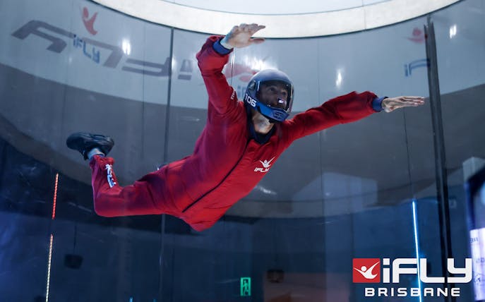 Indoor skydiver in red suit at iFly Brisbane wind tunnel.