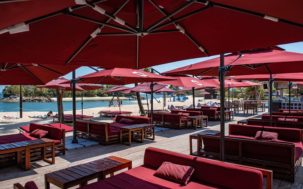 Outdoor dining area with red umbrellas and seating on Sentosa beach, Singapore.