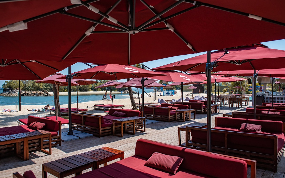 Outdoor dining area with red umbrellas and seating on Sentosa beach, Singapore.