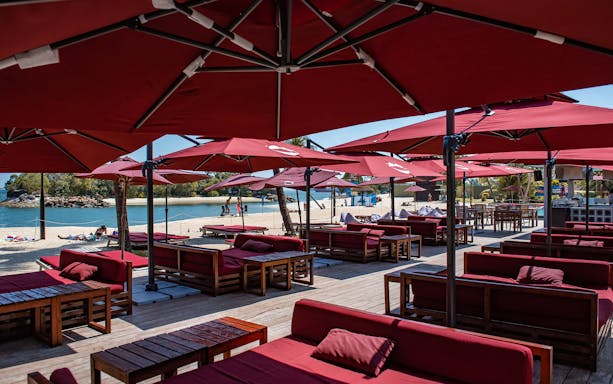 Outdoor dining area with red umbrellas and seating on Sentosa beach, Singapore.