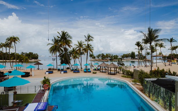 Sentosa beach view with poolside dining area and palm trees.