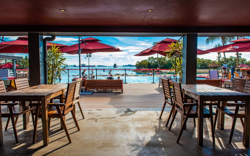 Outdoor dining area overlooking pool and ocean at Sentosa, Singapore.