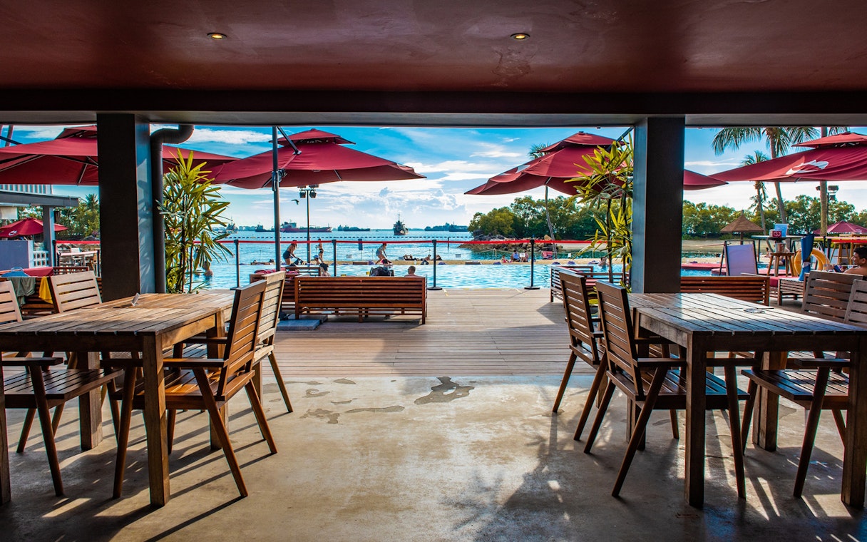 Outdoor dining area overlooking pool and ocean at Sentosa, Singapore.