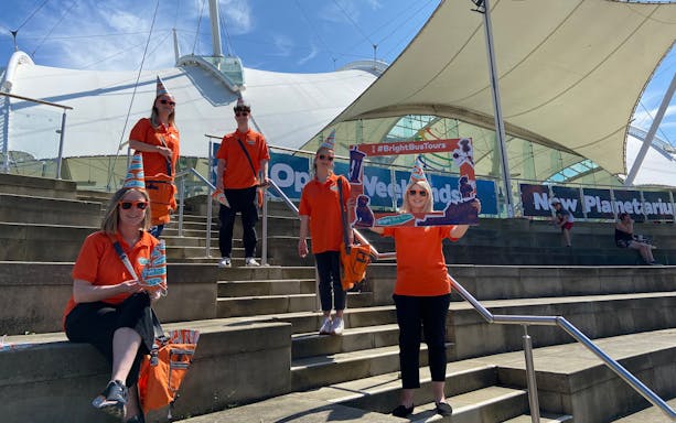 Bright Bus City Tours staff in orange uniforms at a modern outdoor venue.