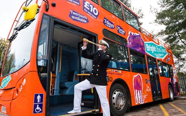 Open-top Bright Bus City Tours bus with a guide in uniform playing a trumpet.
