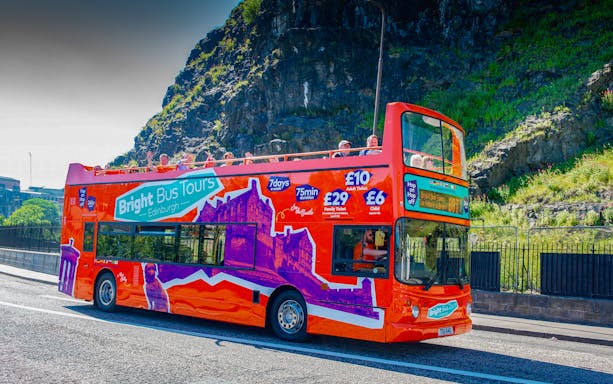 Bright red double-decker bus on Edinburgh tour with passengers waving.