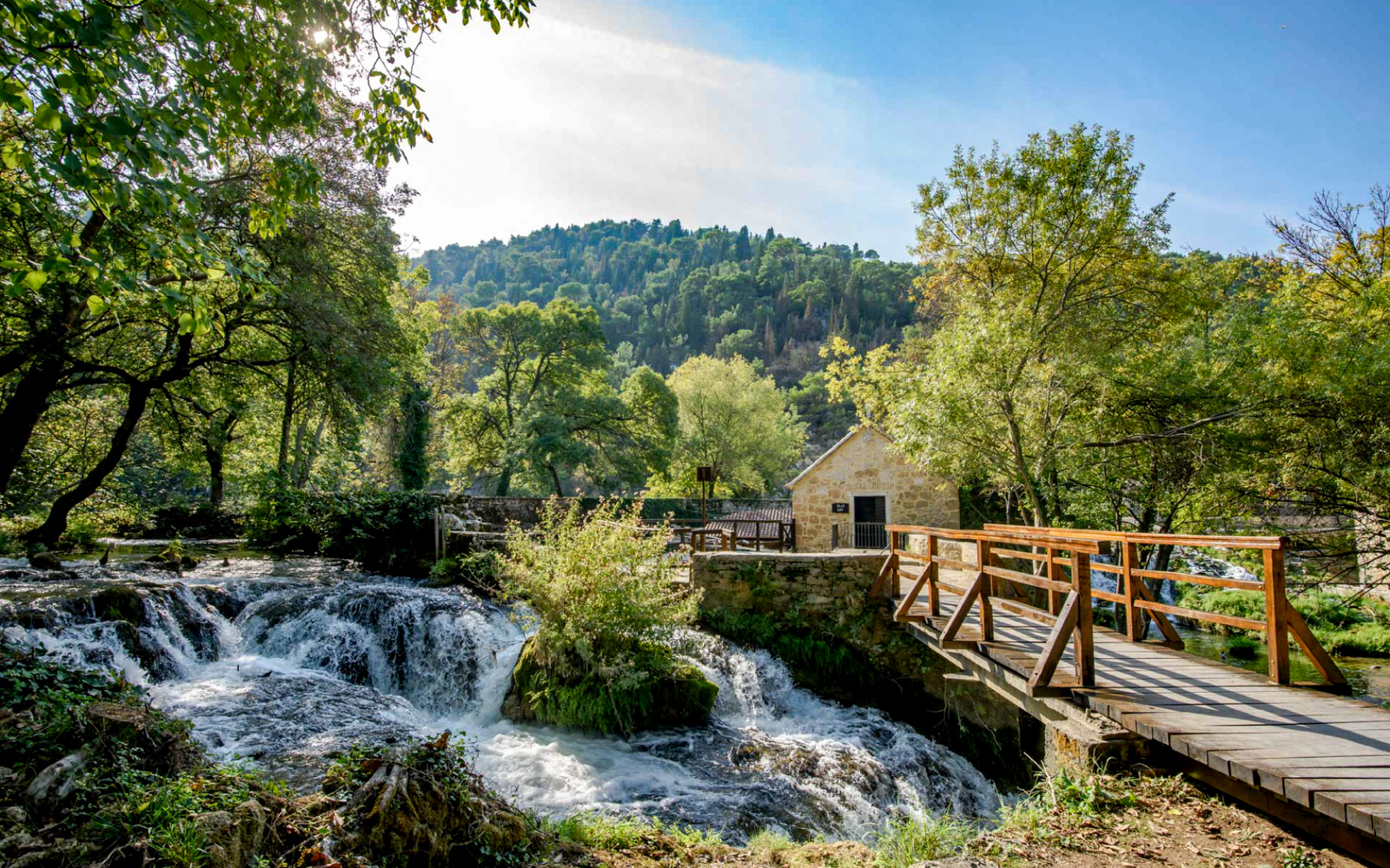 Wooden bridge over Krka waterfalls with lush greenery, part of Split tour.