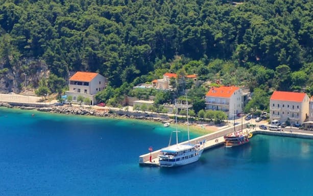 Docked boats at a pier on Korcula Island, surrounded by lush greenery and coastal buildings.