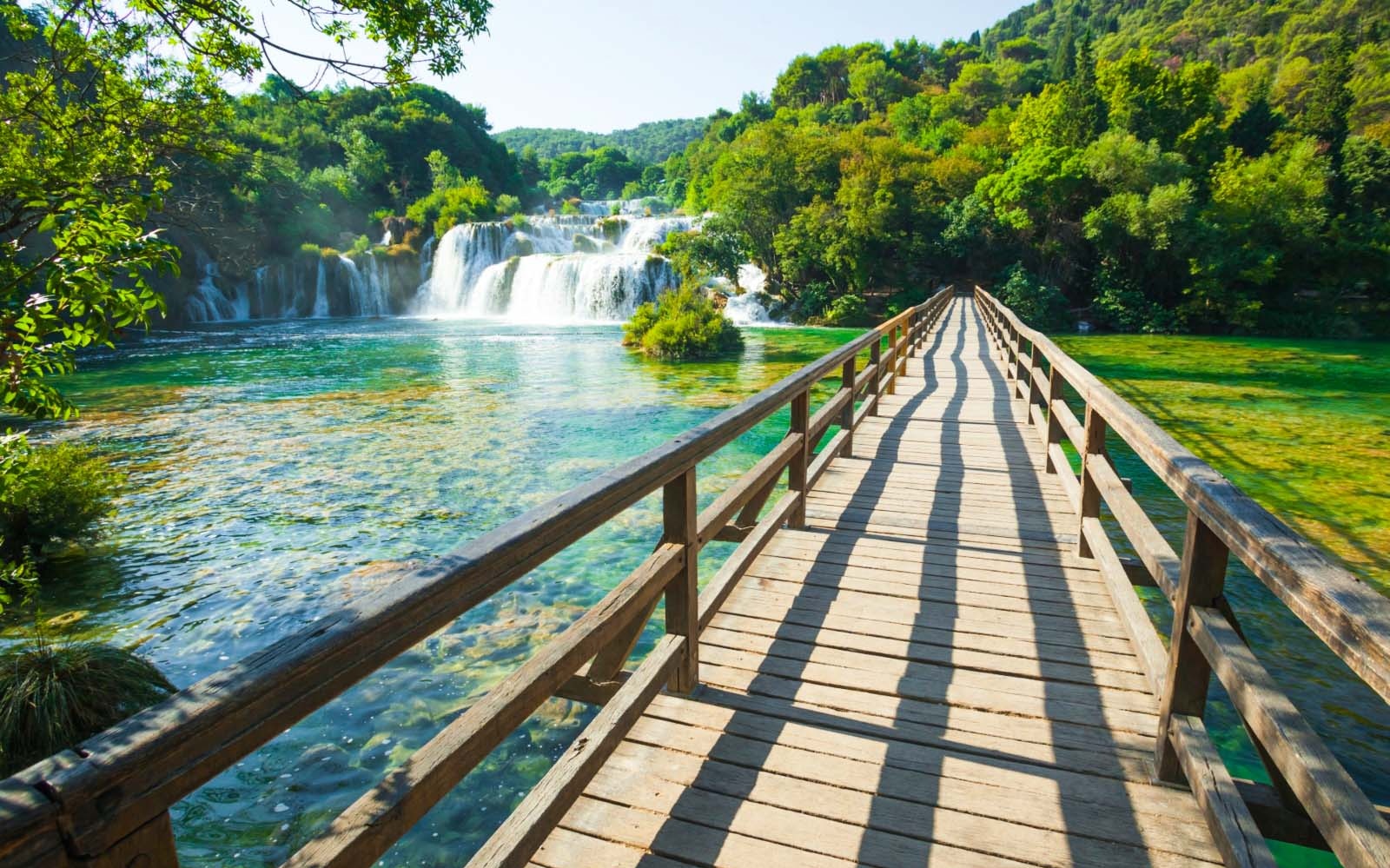Wooden bridge over clear water with waterfalls in Krka National Park, Croatia.