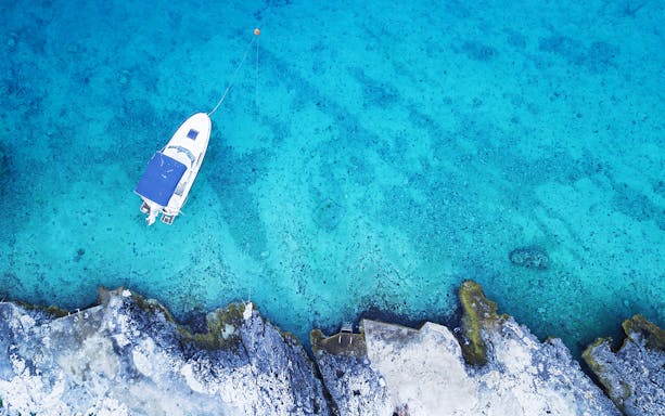 Boat anchored near rocky shore in clear blue waters, Blue Cave tour, Hvar and Five Islands from Split.