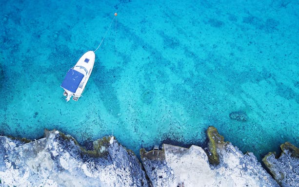 Boat anchored in clear blue waters near rocky shore, Blue Lagoon half-day tour.