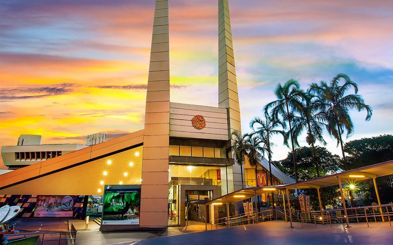 Science Centre entrance with tall structures and palm trees at sunset.