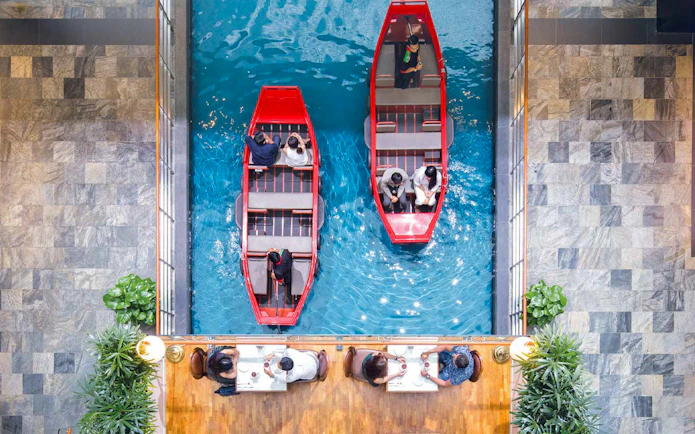 Sampan boats on indoor canal at Marina Bay Sands, Singapore, with diners nearby.